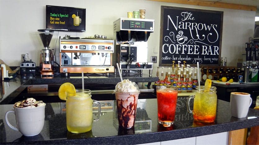 A variety of colorful beverages are displayed on a counter at The Narrows Coffee Bar, with a coffee machine in the background.