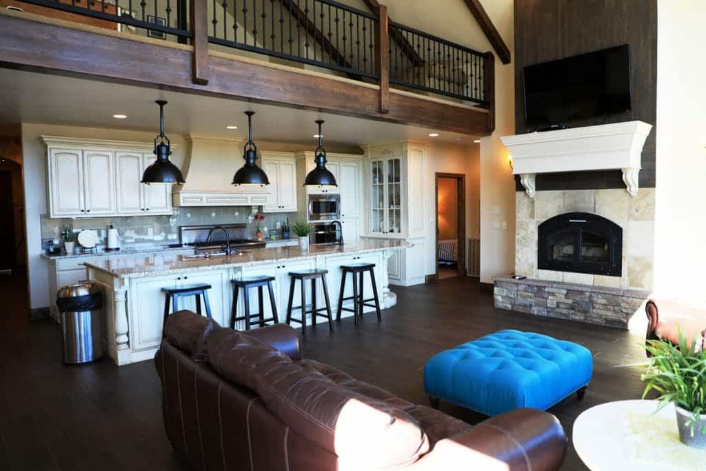 A modern open-concept kitchen and living room with wooden beams, a fireplace, and a blue ottoman.
