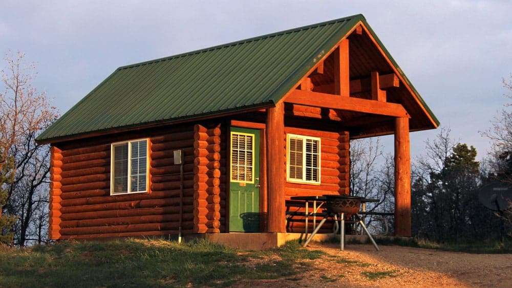 A small log cabin with a green metal roof and a porch.