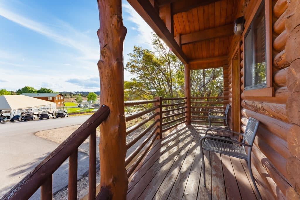 A wooden porch with two chairs and a view of a grassy area and buildings in the distance.