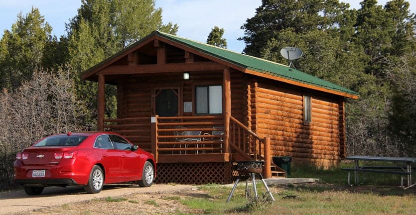 A cozy log cabin with a green roof and a red car parked in front.