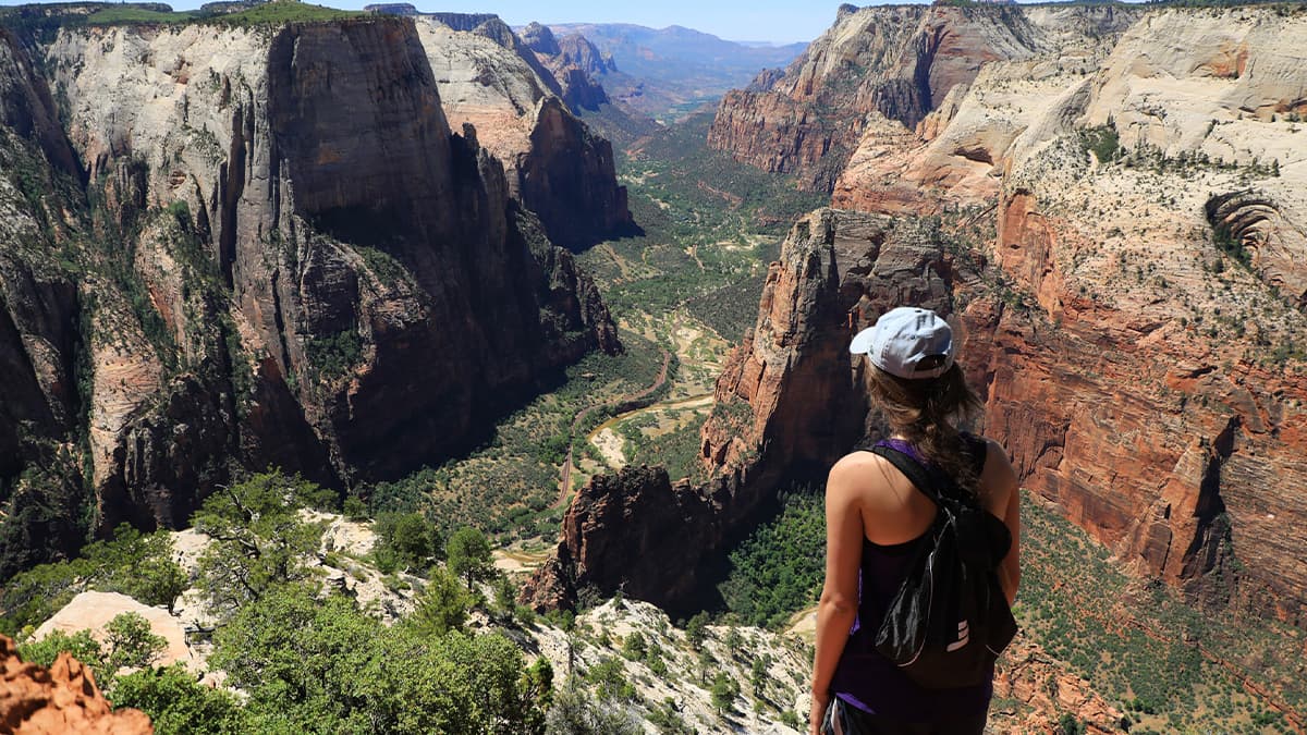 A person stands on a rocky ledge overlooking a vast canyon landscape.