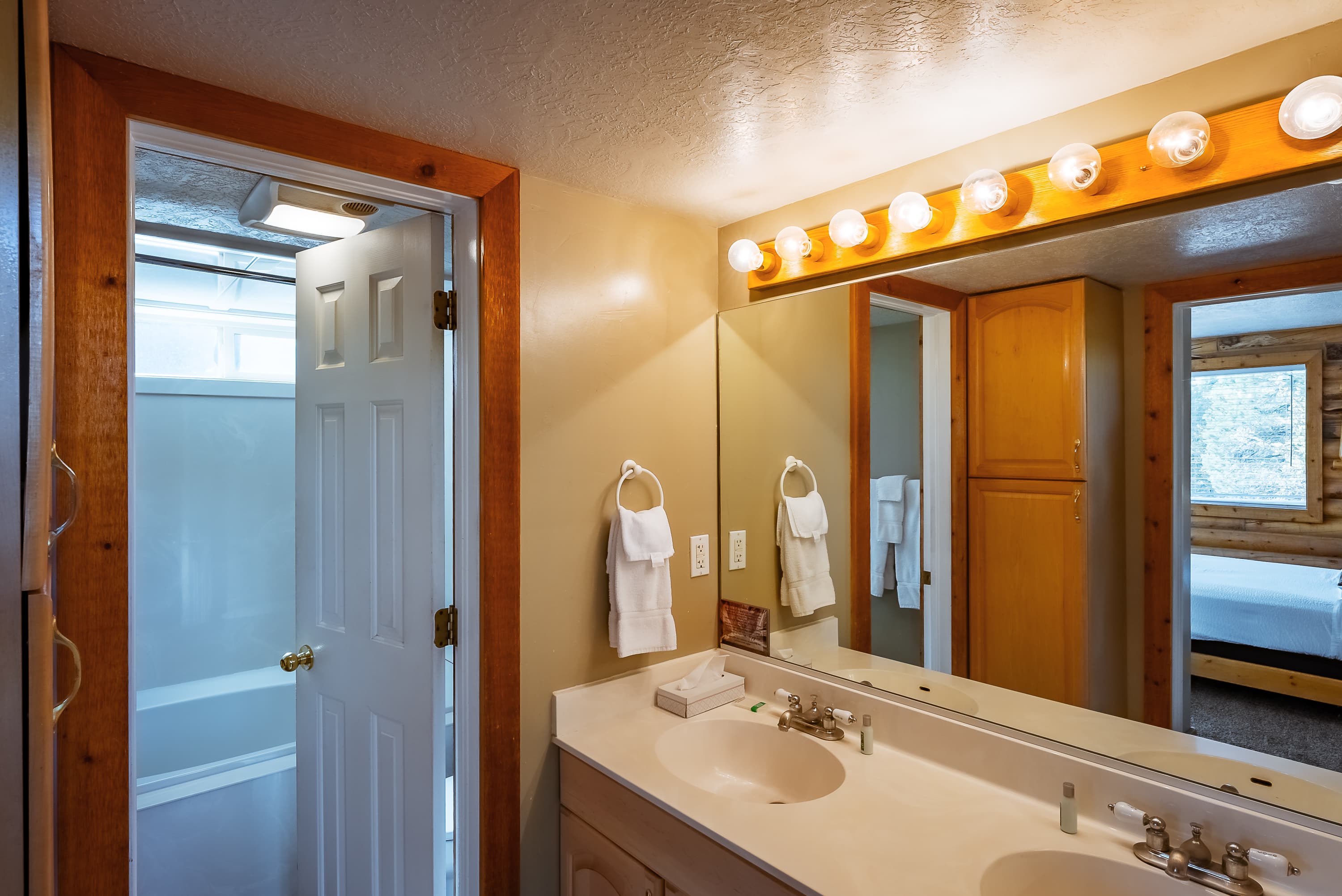 Brightly lit bathroom featuring a double vanity, towels, and a shower visible through an open door.