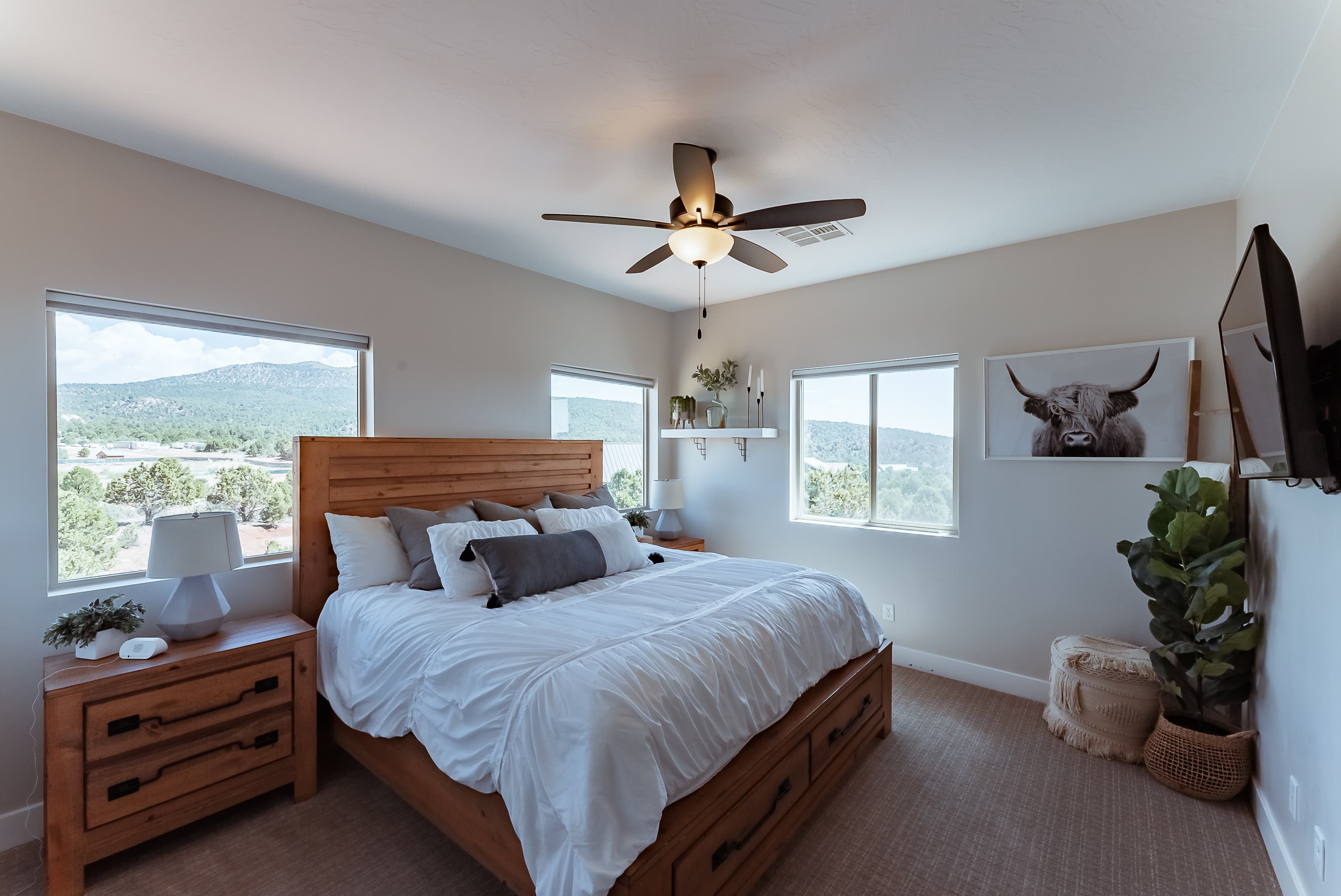 Bright and airy bedroom featuring a wooden bed, greenery, and mountain views.