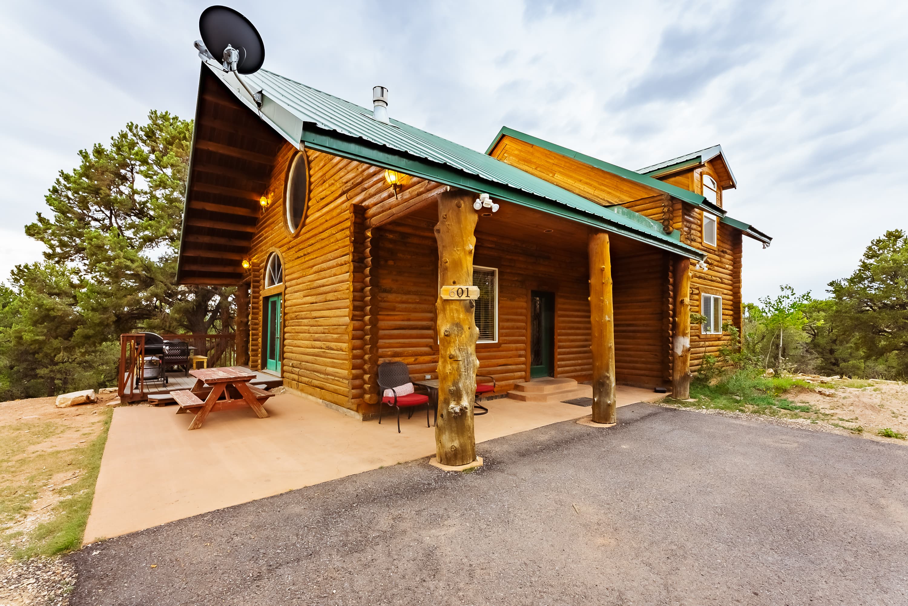 A log cabin house with a green roof and porch set in a natural landscape.