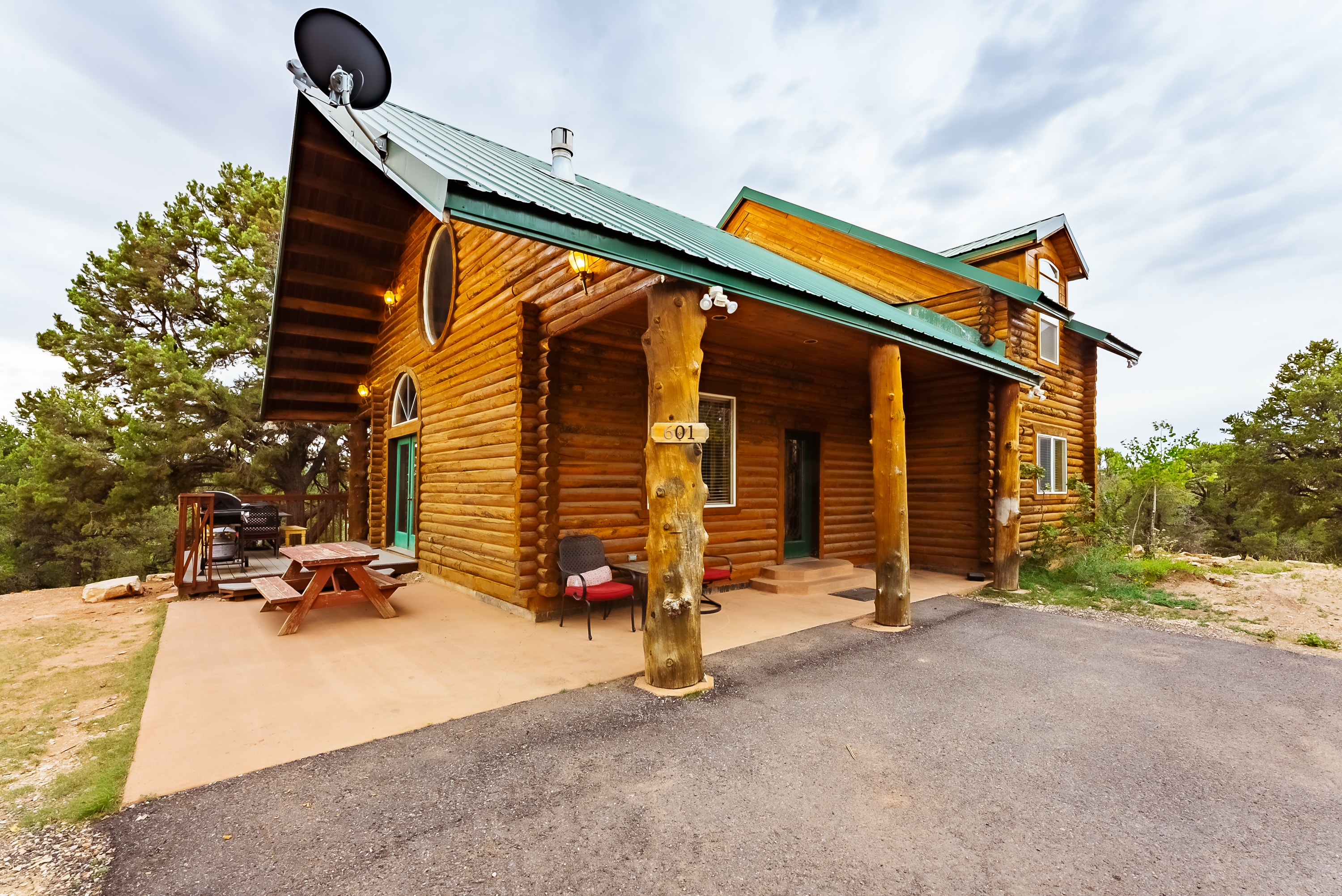 A log cabin house with a green roof and porch set in a natural landscape.