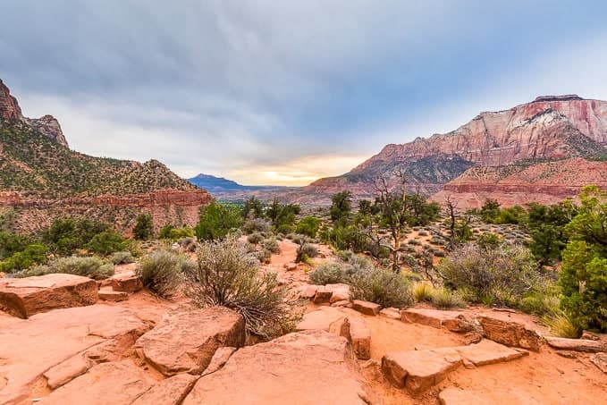 A scenic view of rugged red rock formations and desert vegetation under a cloudy sky.