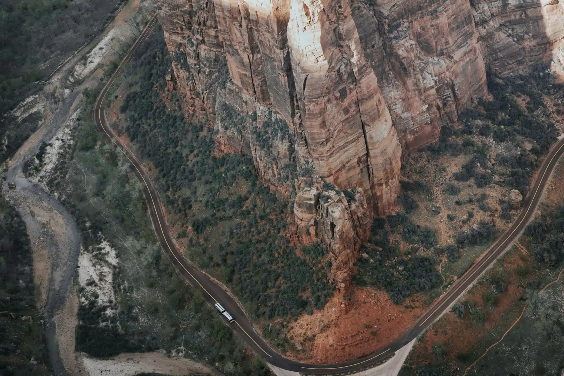 Aerial view of a winding road alongside steep, reddish cliffs and greenery.