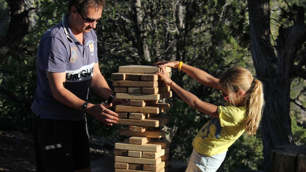 A man and a girl play together, carefully stacking wooden blocks outdoors.