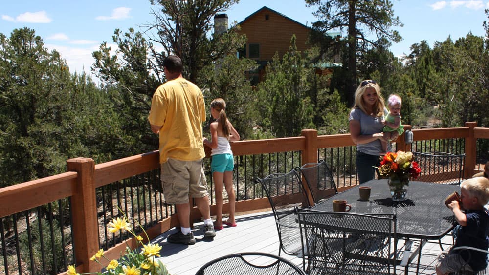 A family enjoys a sunny outdoor patio with trees and a house in the background.