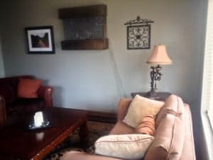 Cozy living room featuring a beige couch, red accent chair, decorative wall art, and a lamp.