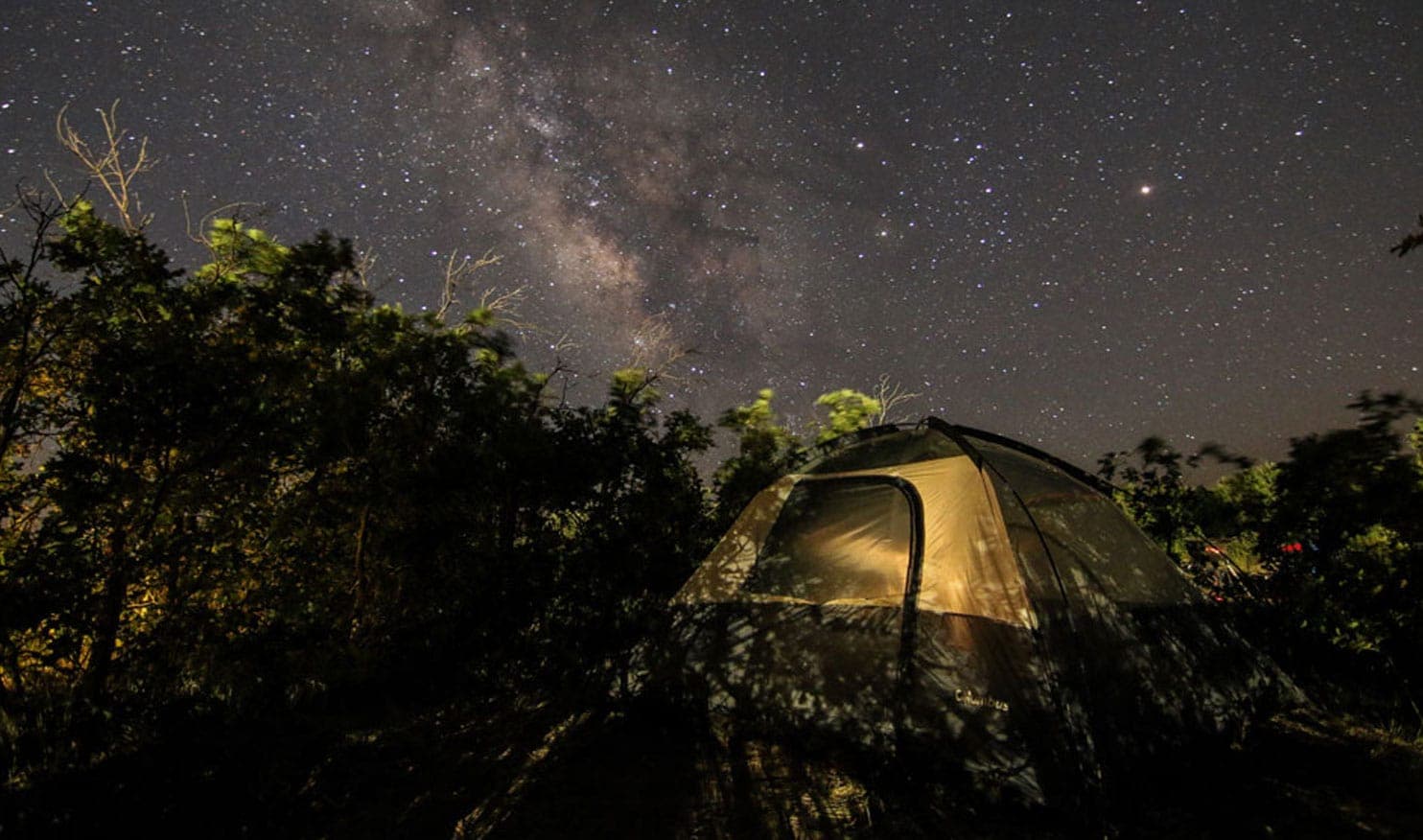 A tent illuminated under a starry night sky filled with the Milky Way.