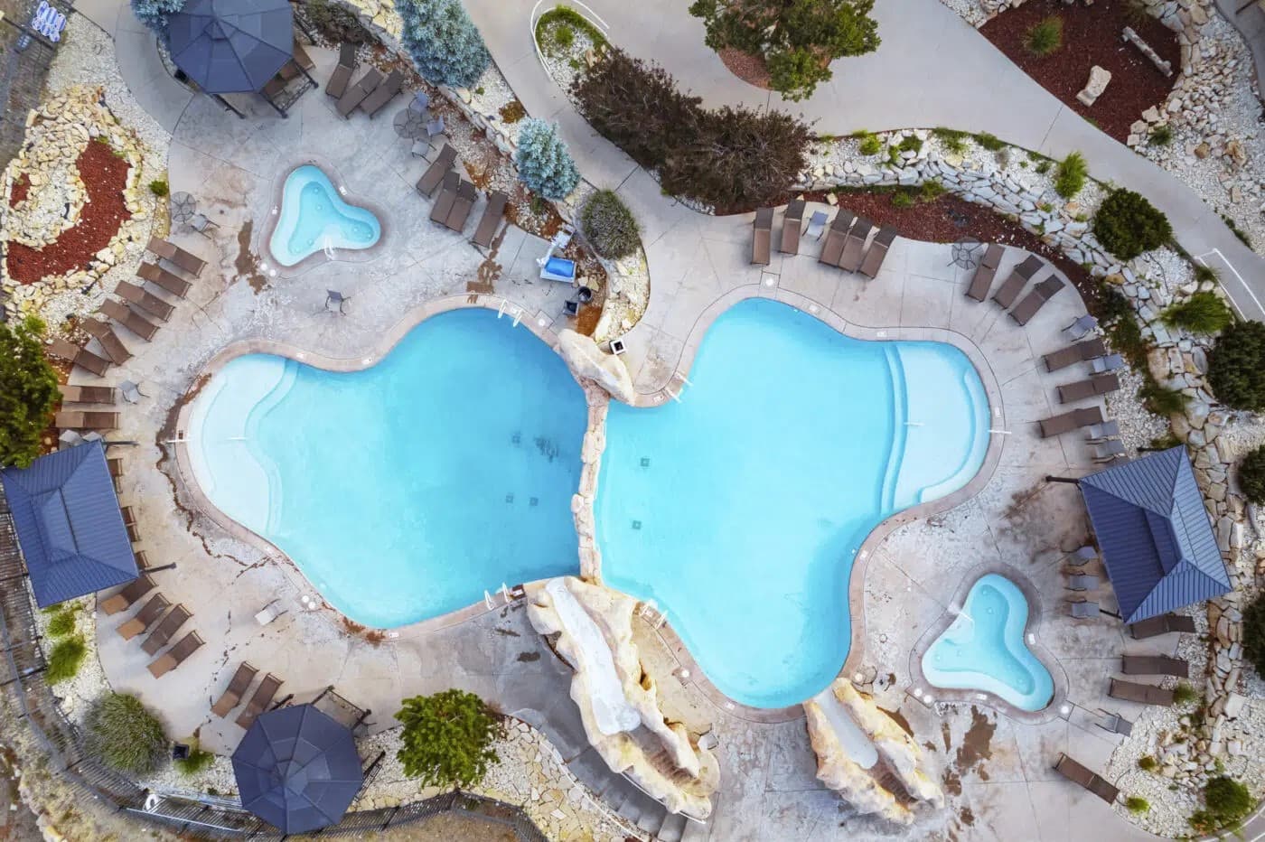 Aerial view of two interconnecting swimming pools surrounded by lounge chairs and landscaping.