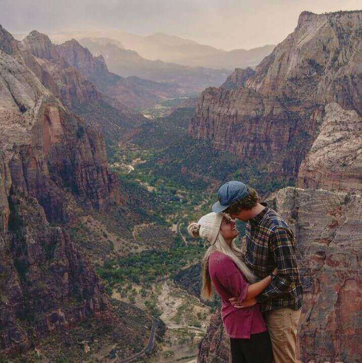 A couple kisses on a cliff overlooking a vast canyon landscape.