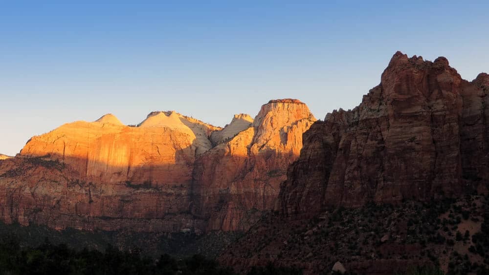 Golden sunlight illuminates rocky cliffs against a clear blue sky.