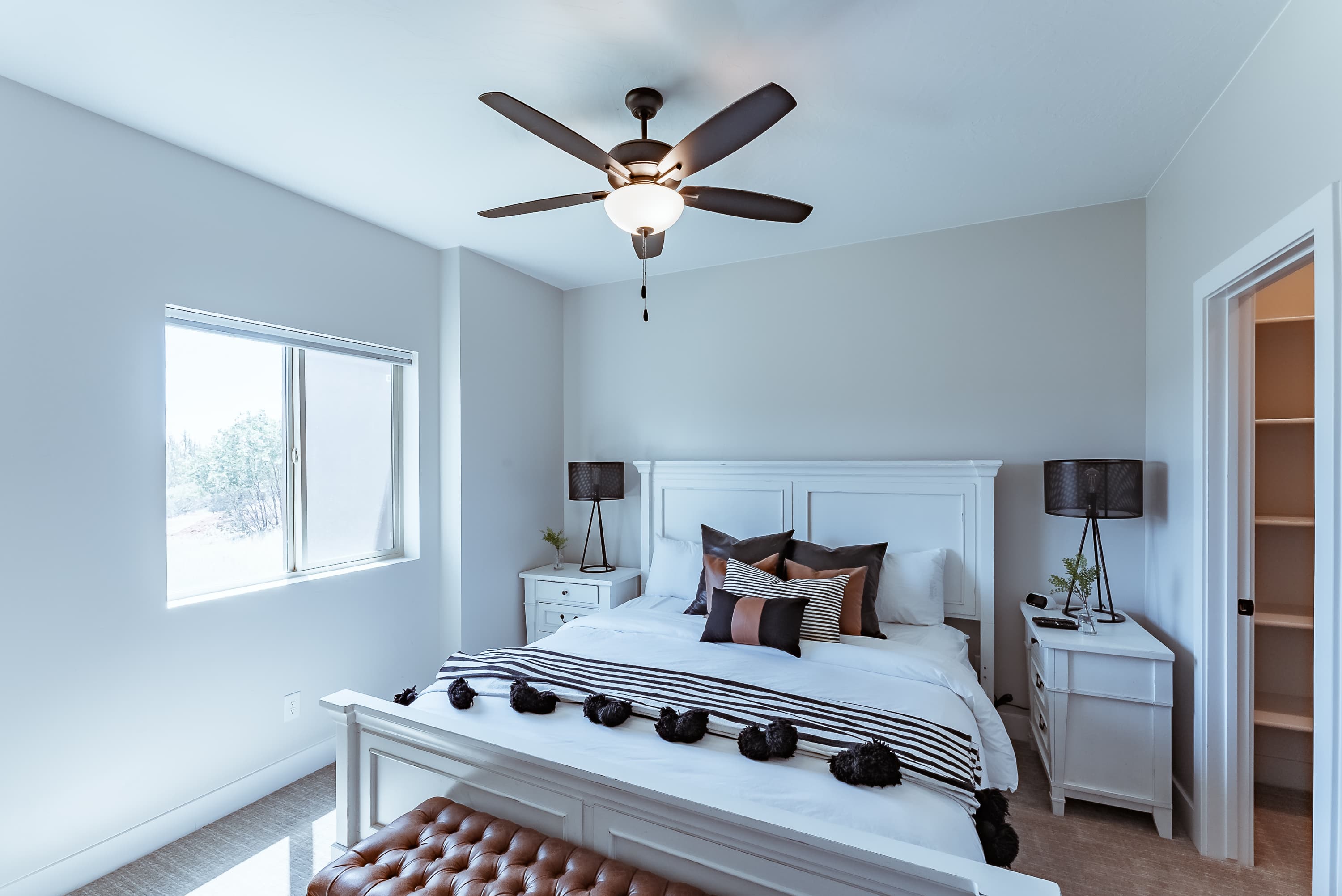 Bright, modern bedroom featuring a white bed, decorative pillows, and a ceiling fan.
