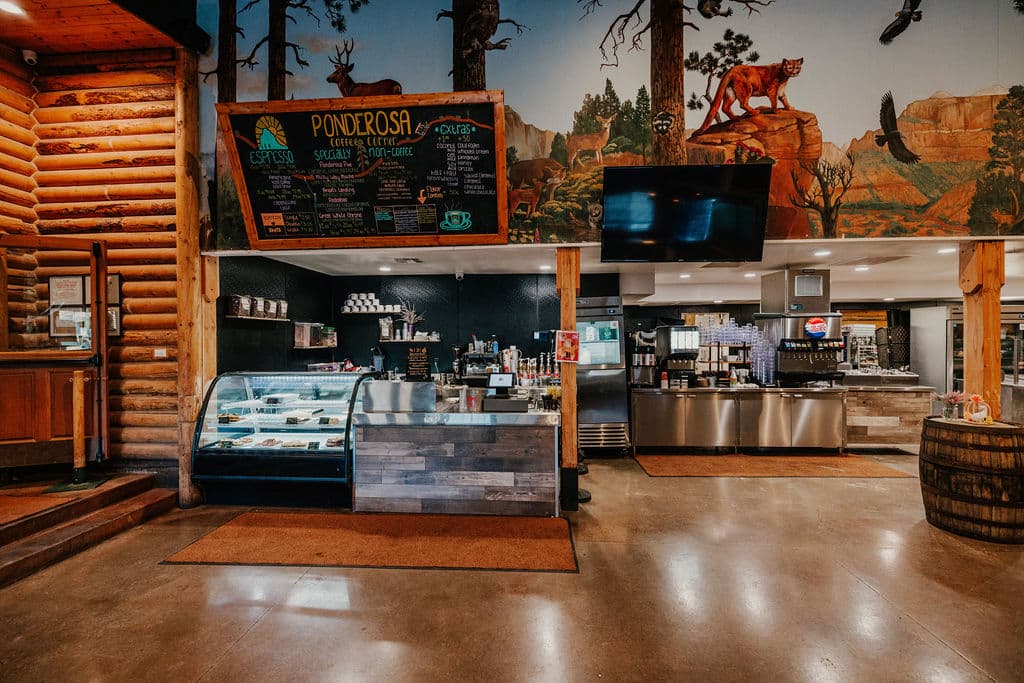 Cozy café interior featuring a log cabin design, a large mural, and a display case with desserts.