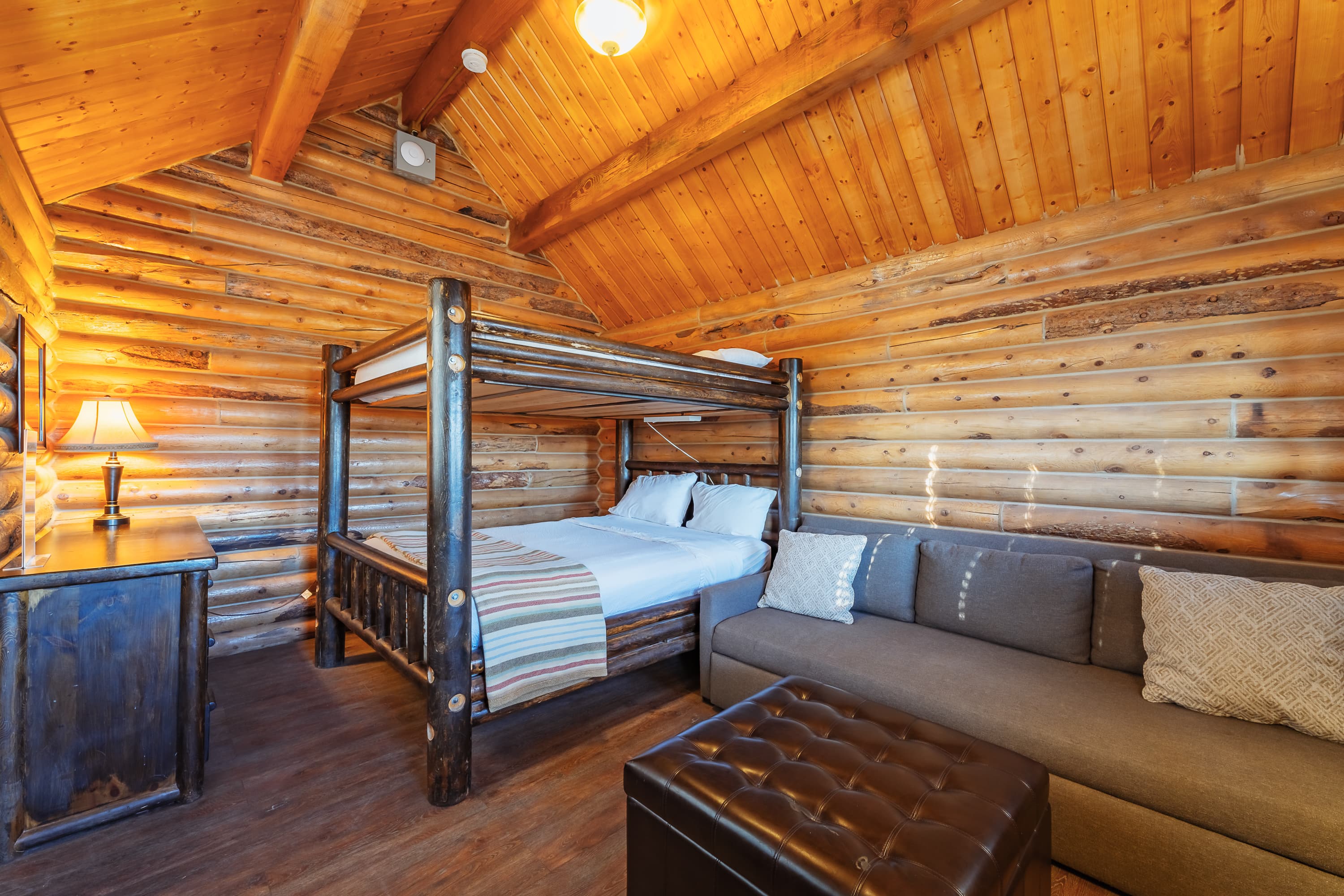 A cozy wooden cabin interior featuring a bunk bed, a sofa, and warm lighting.