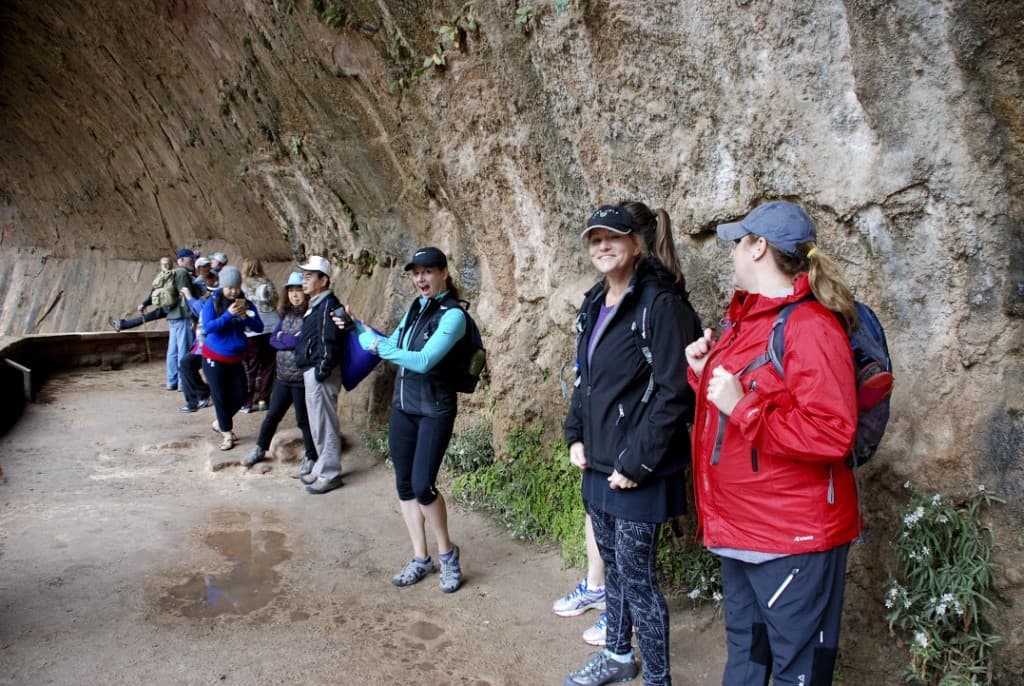 A group of hikers chats and rests against a rocky wall in a scenic location.
