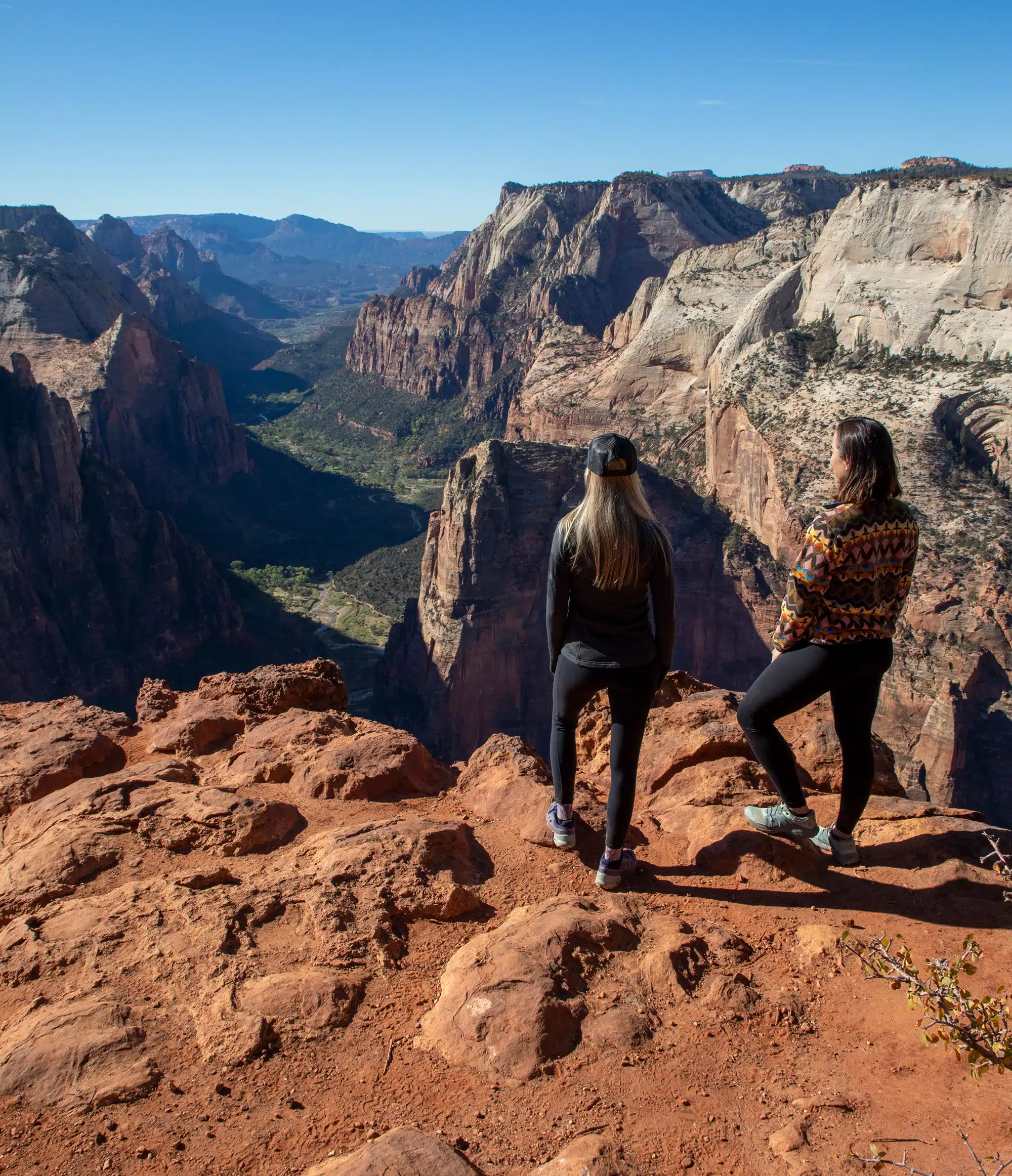 Two people stand atop a rocky cliff, overlooking a majestic canyon landscape.