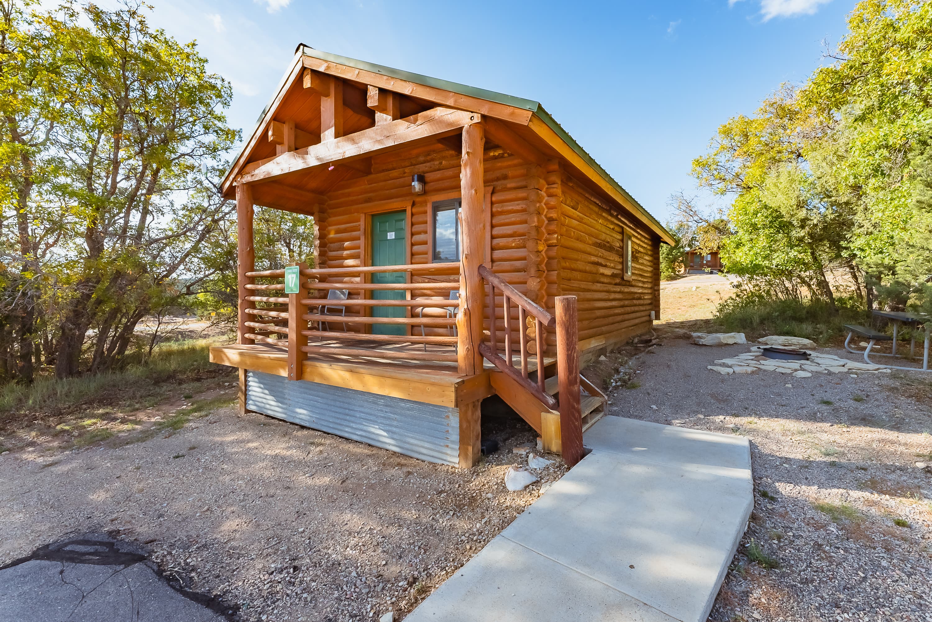 A wooden cabin with a green door and porch surrounded by trees.