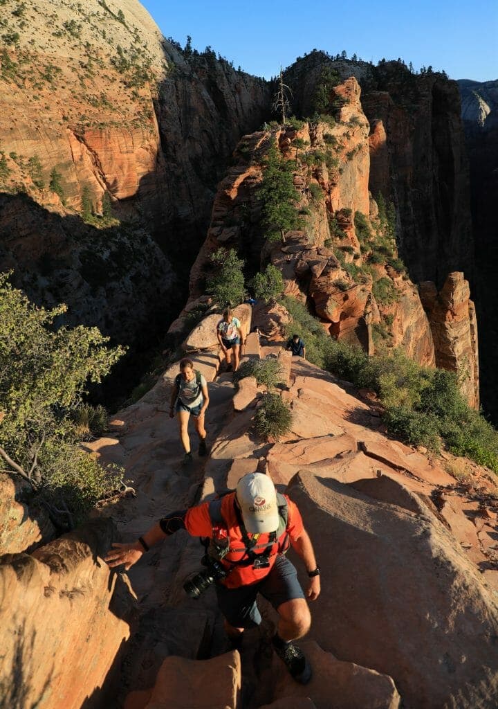 Hikers ascend a narrow rock path surrounded by steep canyon walls.