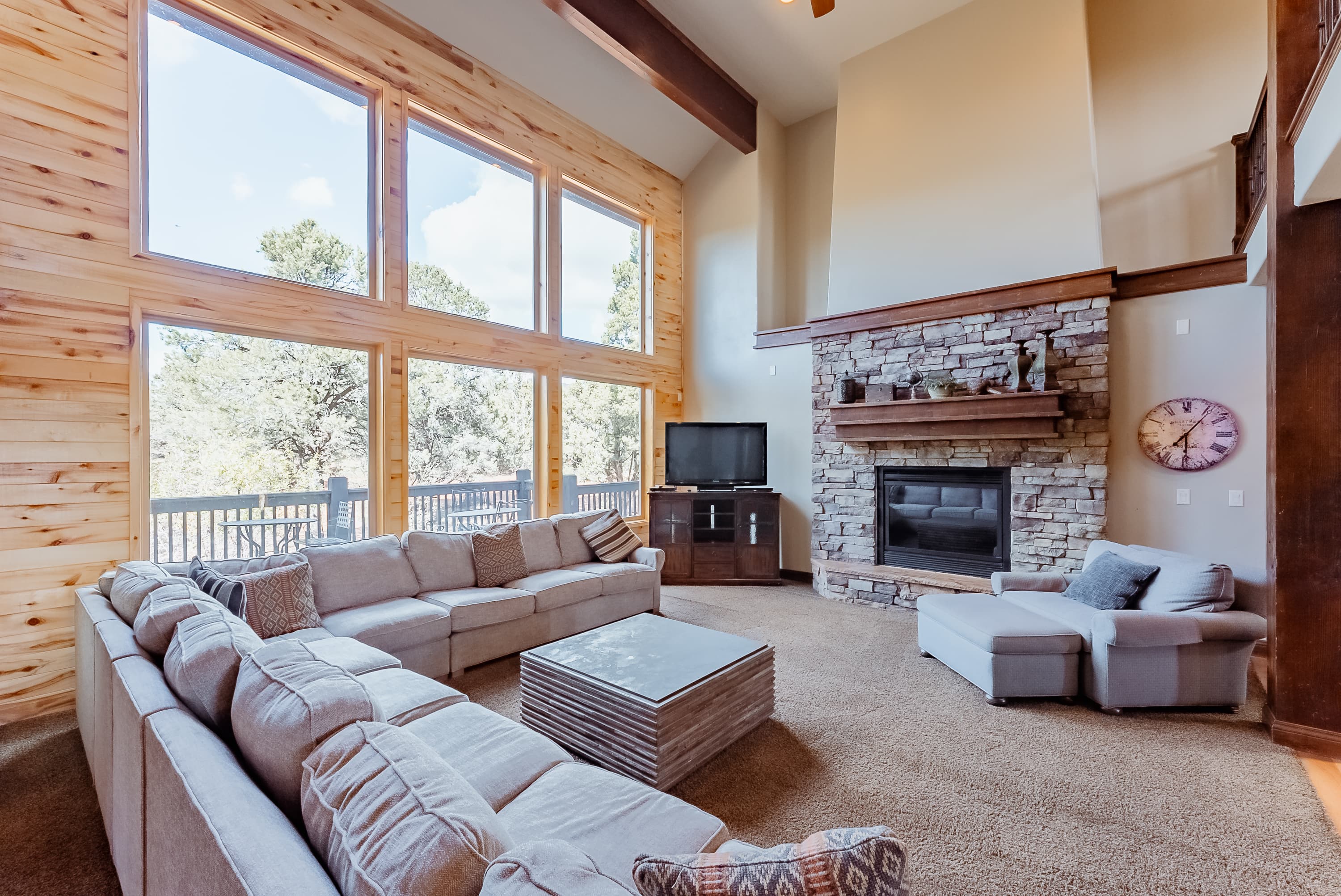 A cozy living room with large windows, a stone fireplace, and a comfortable sectional sofa.