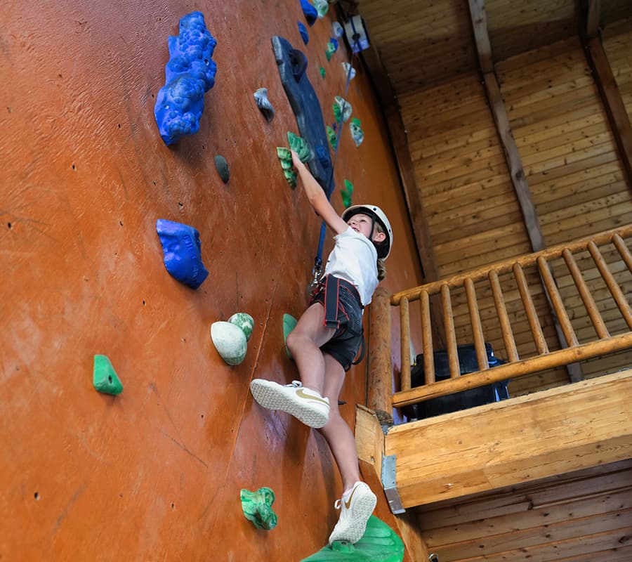 A child in a helmet climbs a colorful indoor climbing wall.