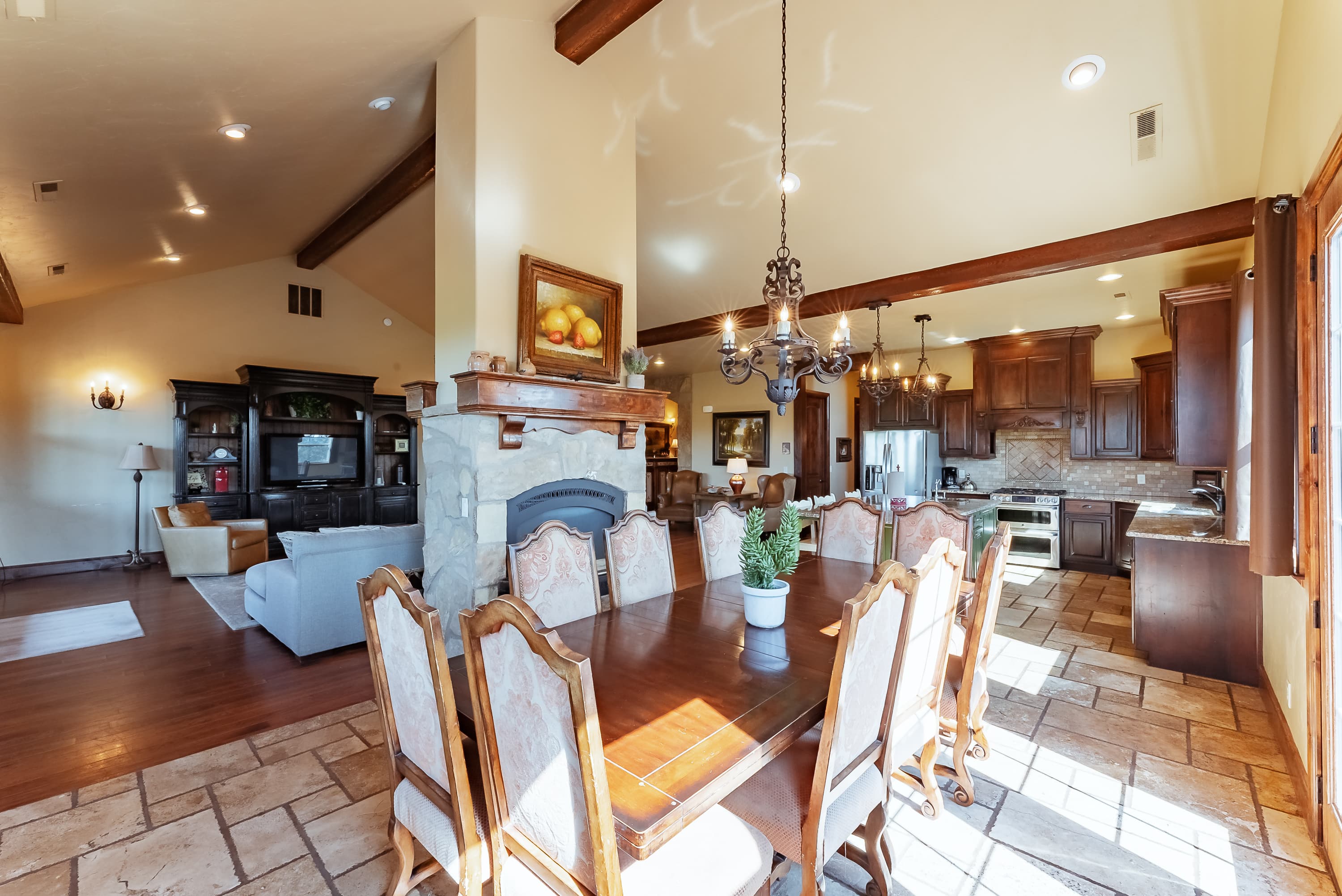A spacious dining area with a wooden table, chairs, a stone fireplace, and a view into a modern kitchen.