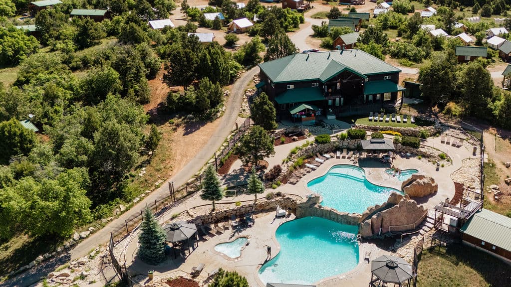 Aerial view of a resort featuring a pool area, surrounded by greenery and cabin-like structures.