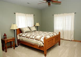 A cozy bedroom featuring a wooden bed, two lamps, and light green walls.