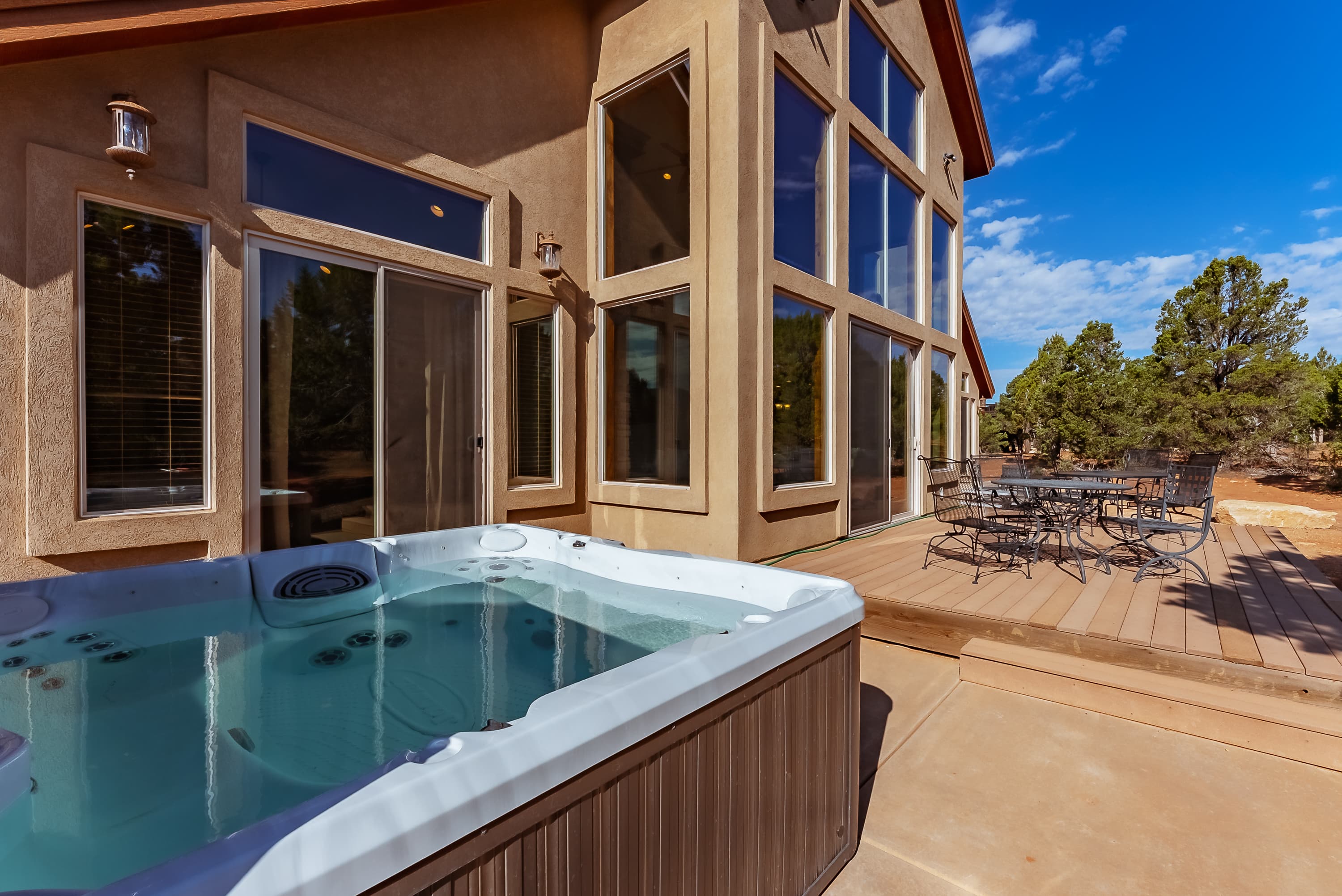 A hot tub sits on a patio beside a large, modern house with expansive windows.