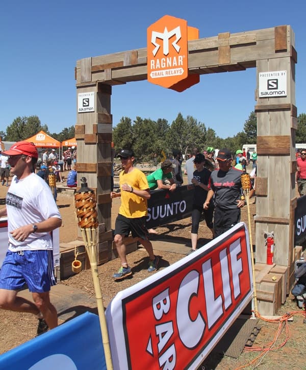 Runners cross the finish line at a Ragnar Trail Relay event under a wooden archway.