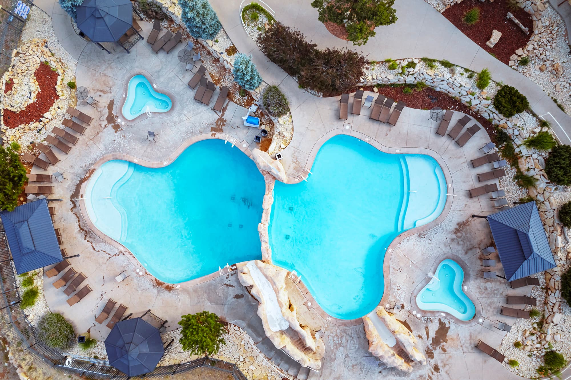 Aerial view of a resort-style pool area with two interconnected pools, surrounded by lounge chairs and landscaped gardens.