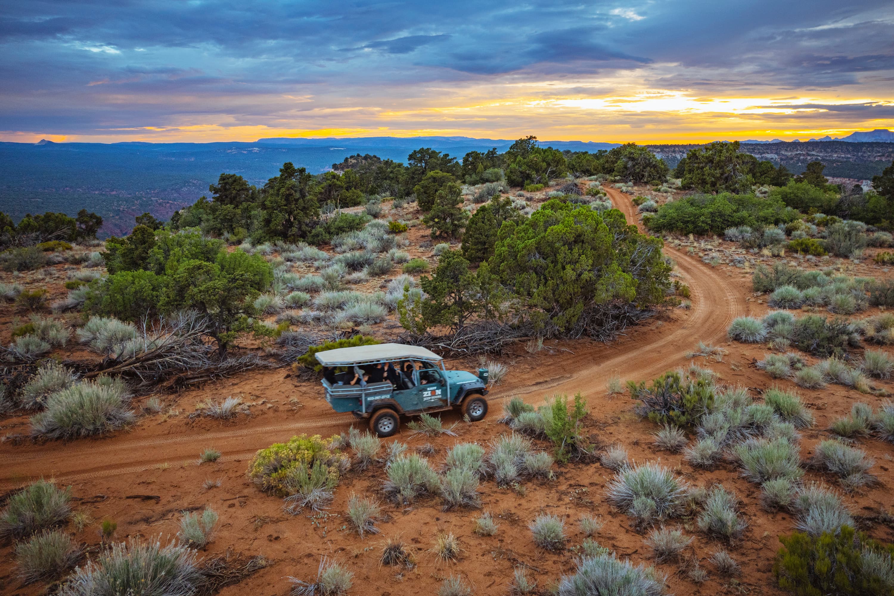 A four-wheel drive vehicle navigates a winding dirt road amidst a scenic desert landscape at sunset.