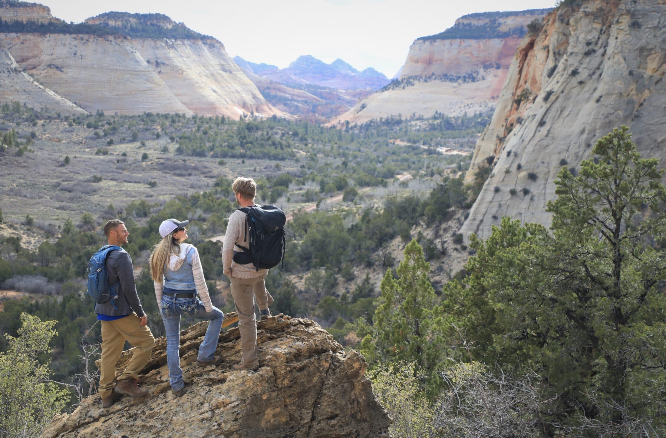 Three hikers stand on a rocky outcrop, overlooking a vast canyon landscape.