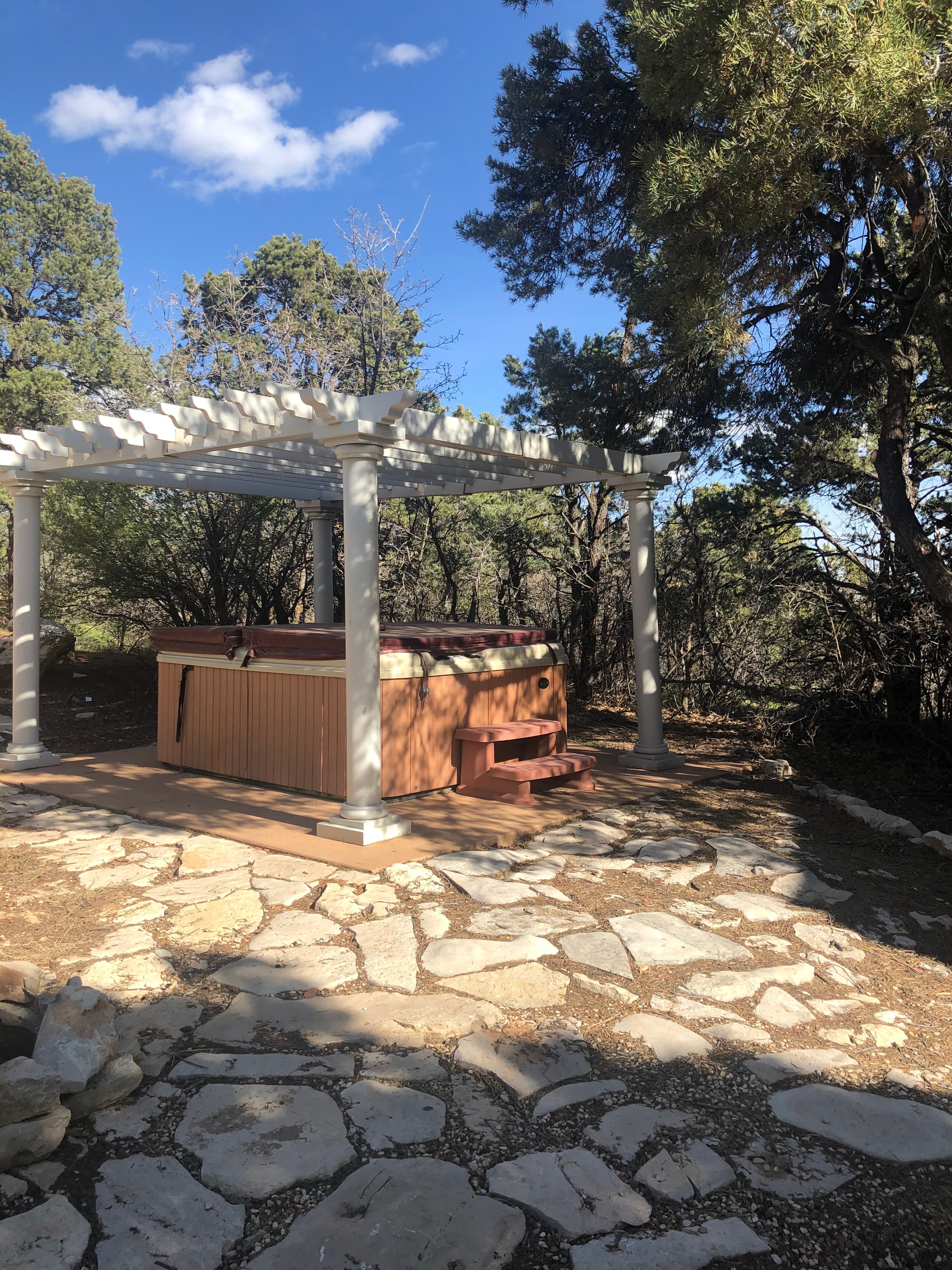 A hot tub under a pergola surrounded by trees and a stone pathway.
