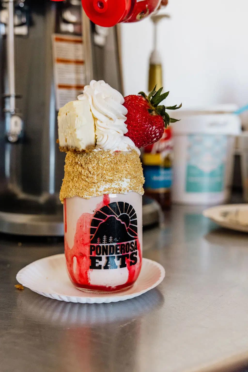 A decorated dessert jar topped with whipped cream, a strawberry, and a slice of cake on a white plate.