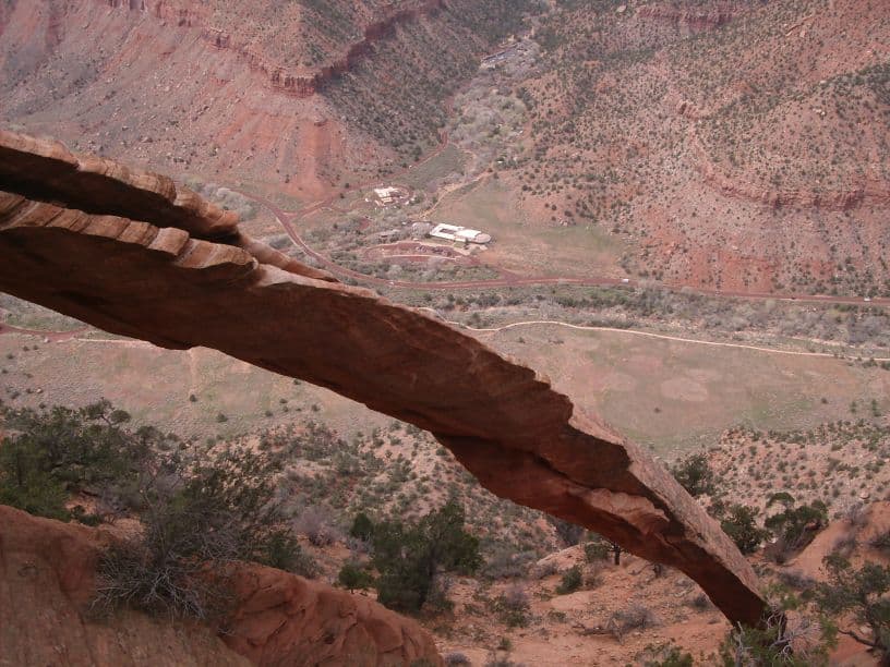 A jagged rock formation extends over a steep canyon with sparse vegetation and a road in the background.