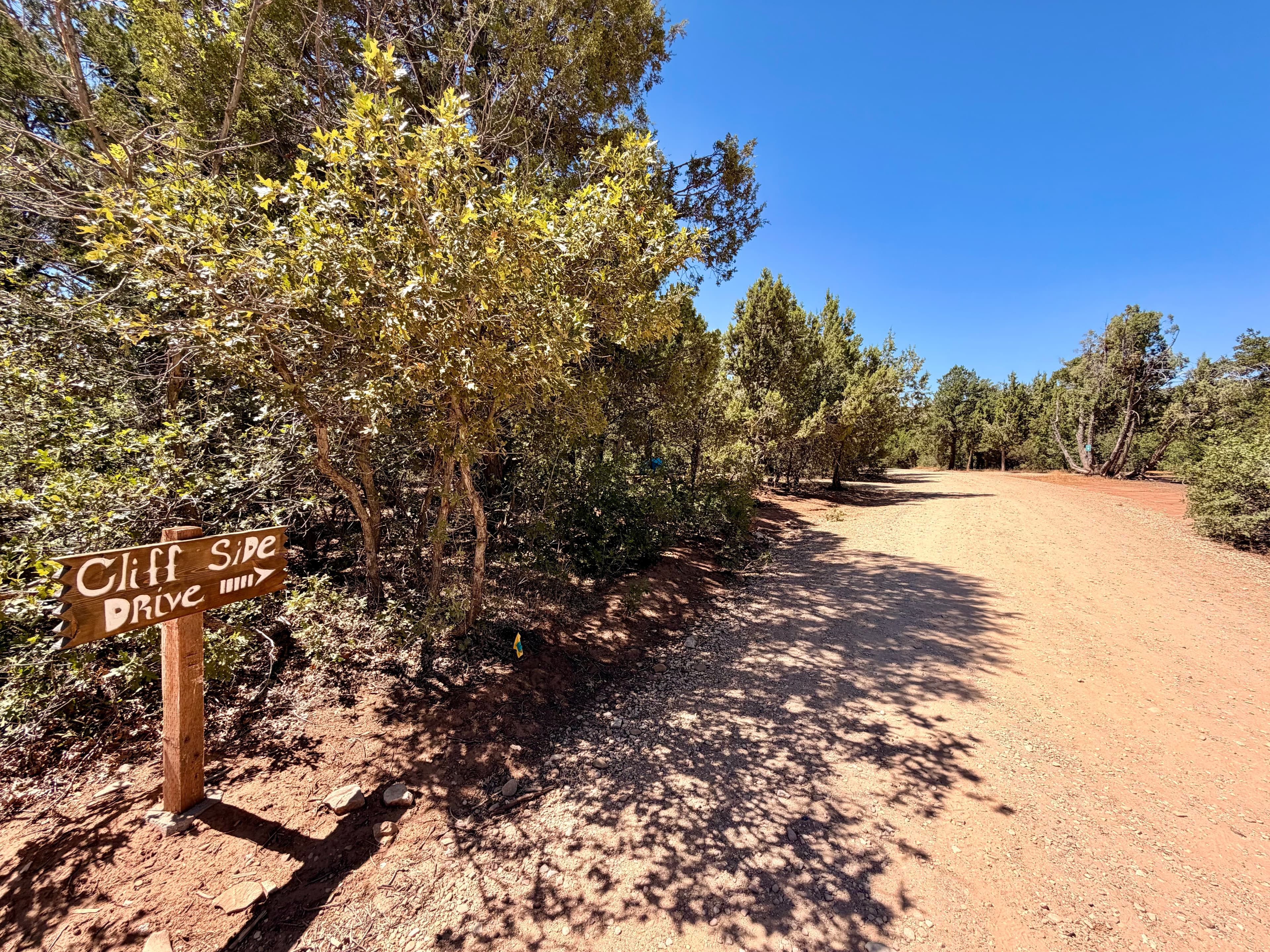 Dirt road marked "Cliff Side Drive" surrounded by greenery under a clear blue sky.