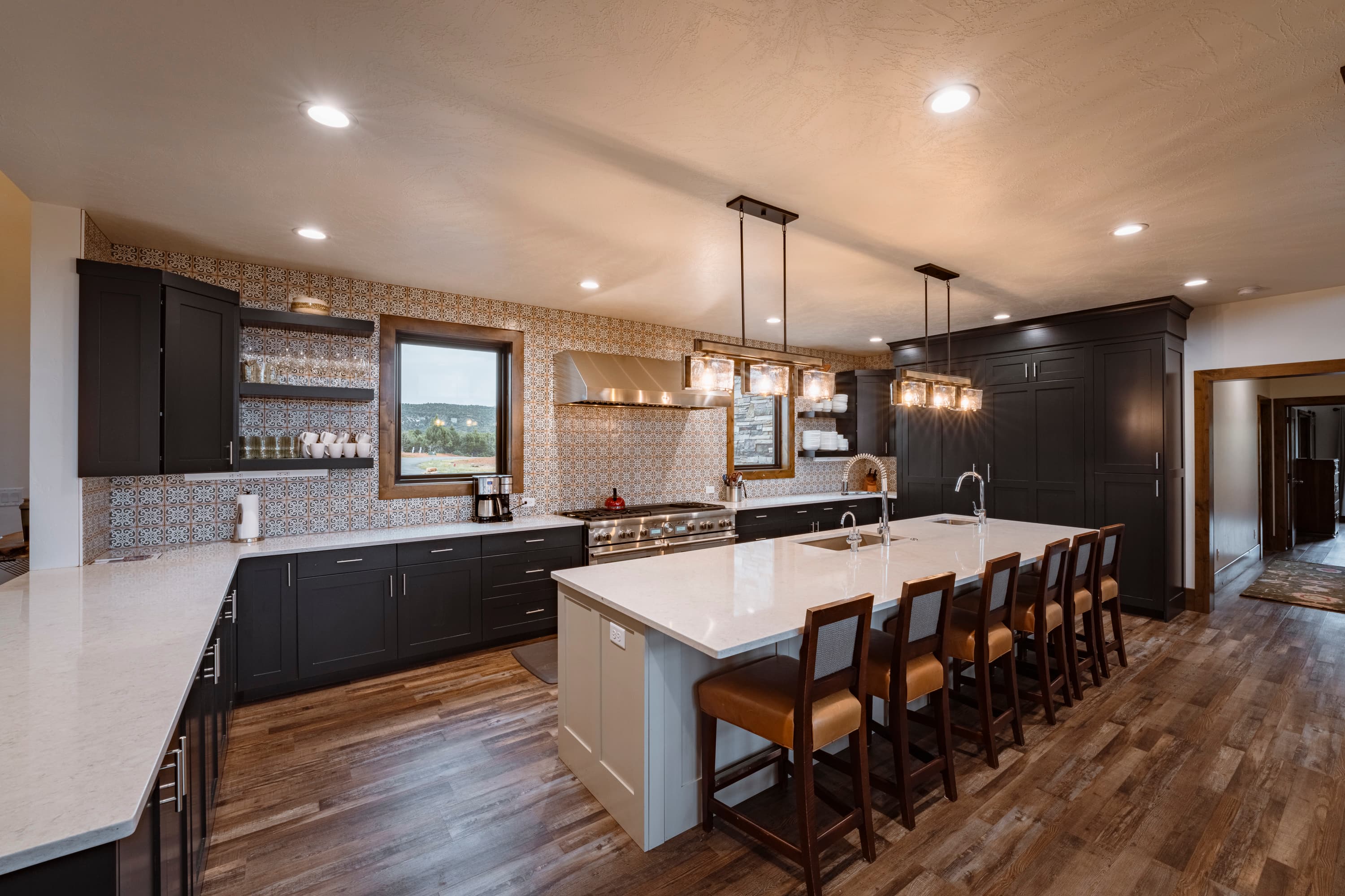 A modern kitchen featuring dark cabinetry, a large central island with seating, and stylish pendant lighting.