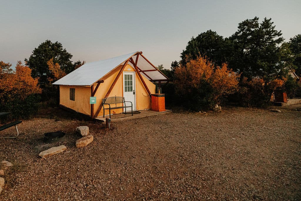 A cozy cabin with a triangular roof surrounded by autumn foliage at dusk.