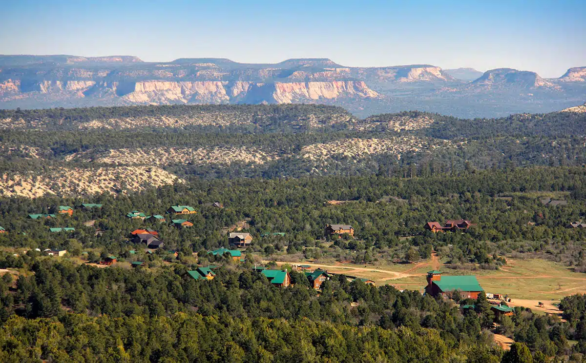 A serene landscape featuring a valley of green trees and rustic homes, with rocky cliffs in the background.