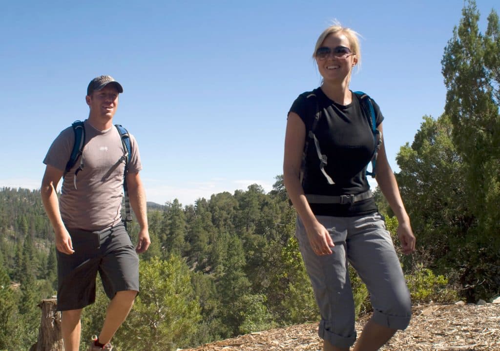 Two hikers walking along a trail surrounded by trees on a sunny day.