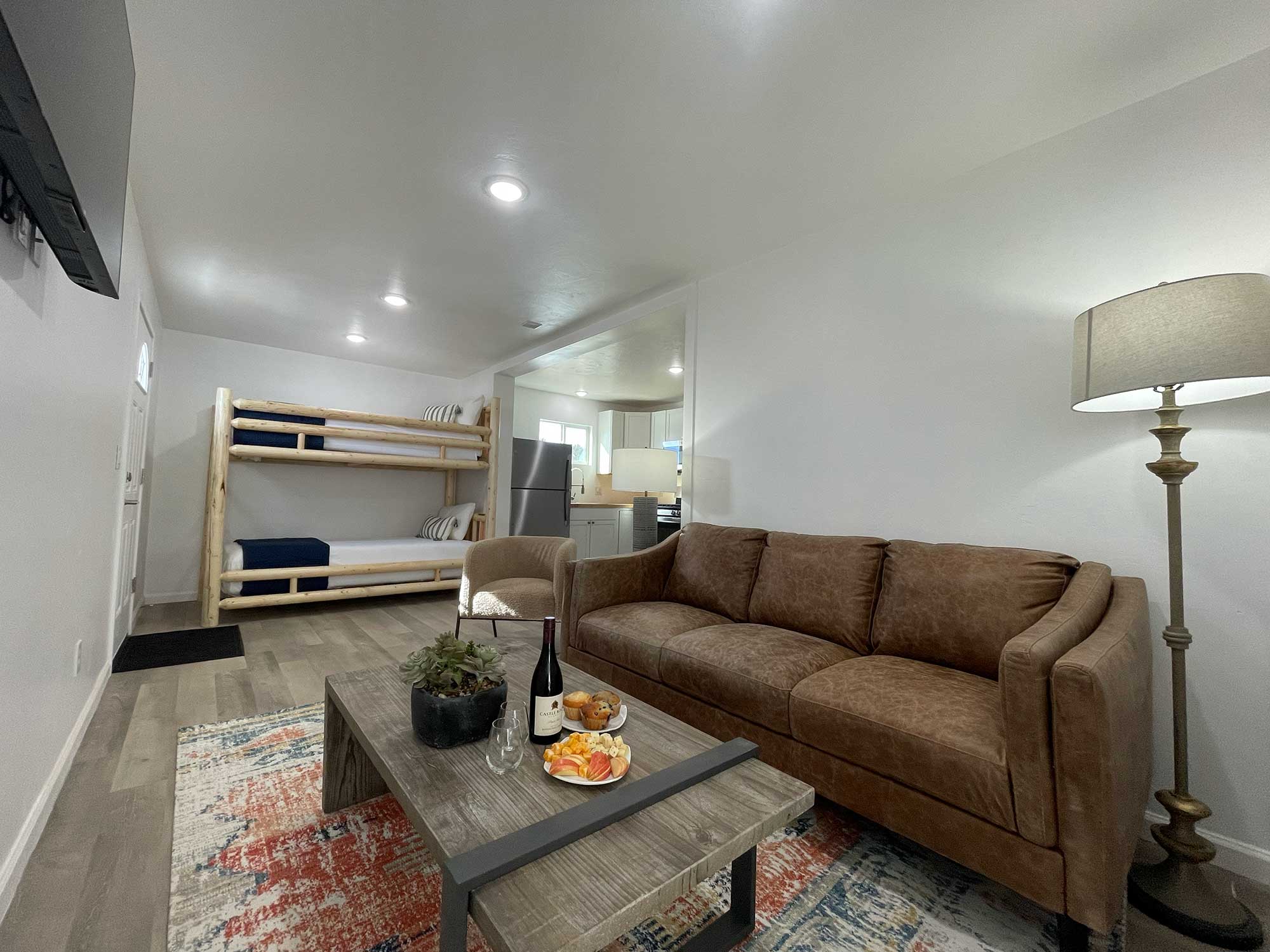 A cozy living area featuring a sofa, a coffee table with snacks, and a set of bunk beds in the background.