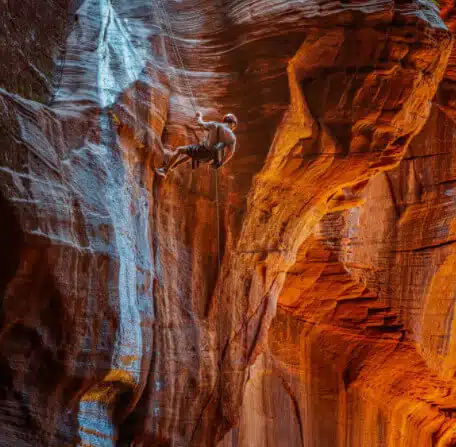 A climber ascends a vibrant rock face in a canyon.