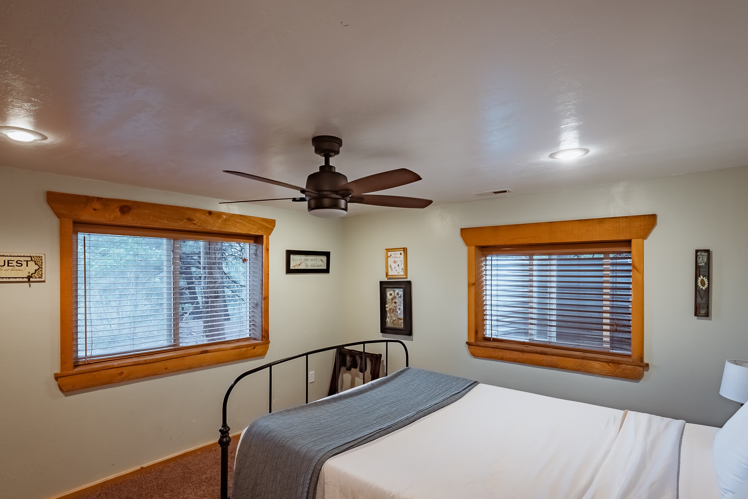 A cozy bedroom featuring a wrought iron bed, natural wood accents, and two windows with blinds.