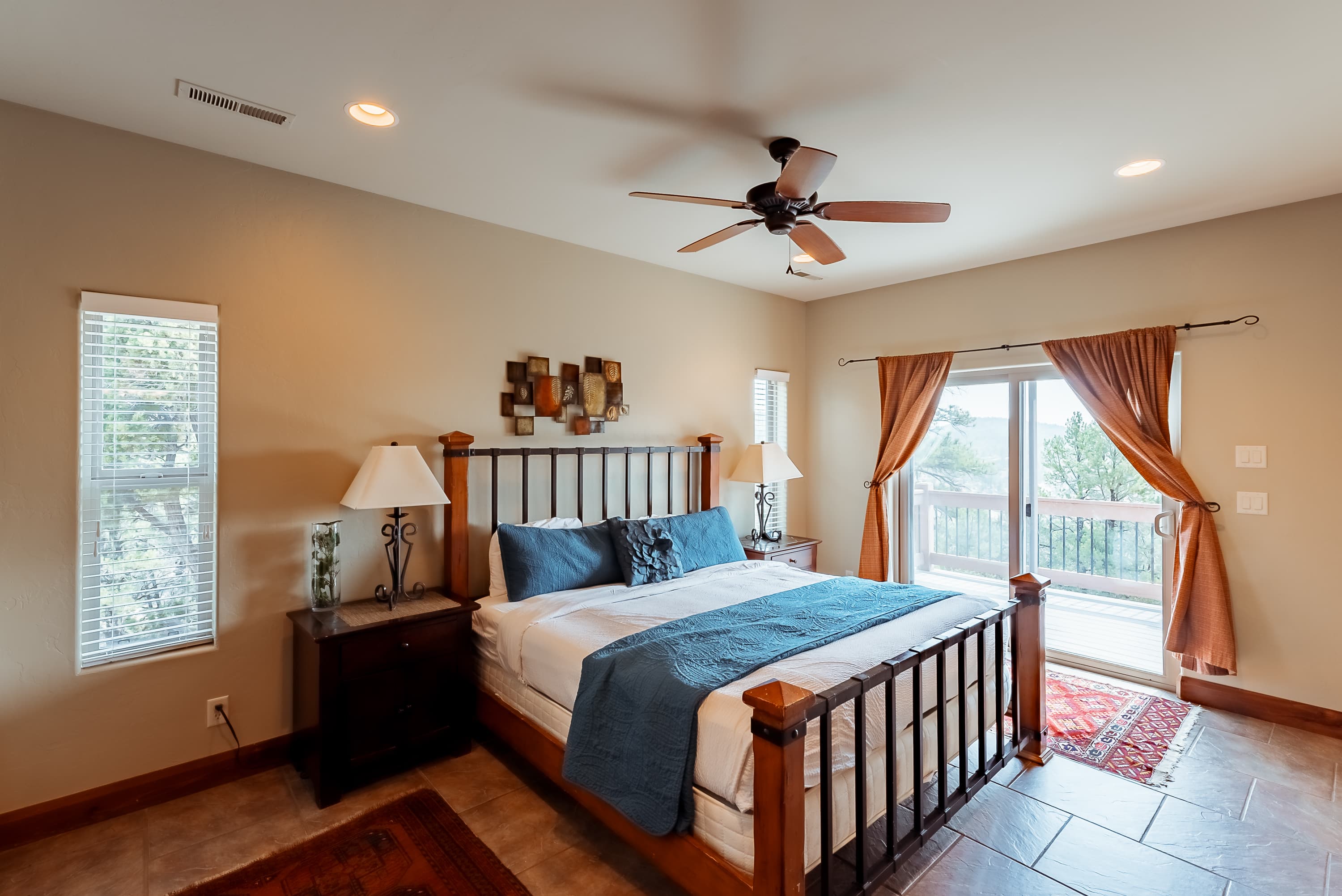 A cozy bedroom with a wooden bed, blue bedding, two lamps, and a sliding glass door leading to a deck.
