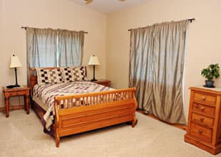 A cozy bedroom featuring a wooden bed, matching nightstands with lamps, and light brown curtains.