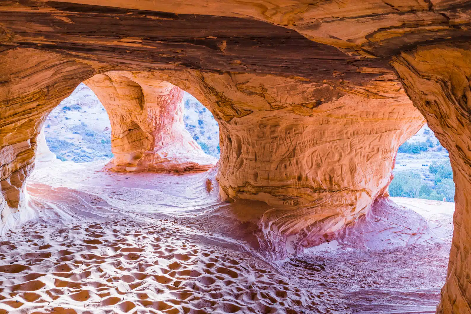 View of a sandstone cave with two openings revealing a bright landscape outside.